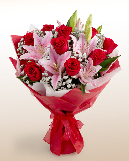Ramo atado a mano de rosas rojas, lirios rosados y gypsophila envuelto en papel rojo con moño rojo