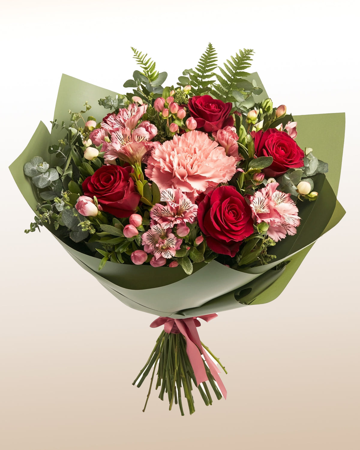 Ramo atado a mano de rosas rojas, claveles y astromelias rosadas con helecho, envuelto en papel verde y cinta rosada