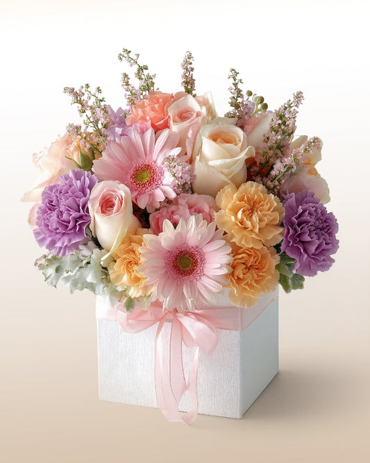 Caja con gerberas, rosas y claveles en tonos suaves. Un arreglo luminoso para celebrar a alguien especial. Envío a domicilio.